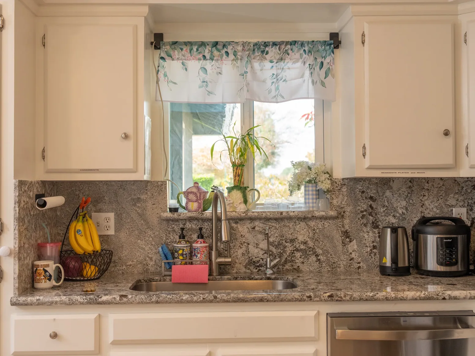 Bright residential kitchen with granite countertops and white cabinetry featuring accessible sink area and natural window lighting