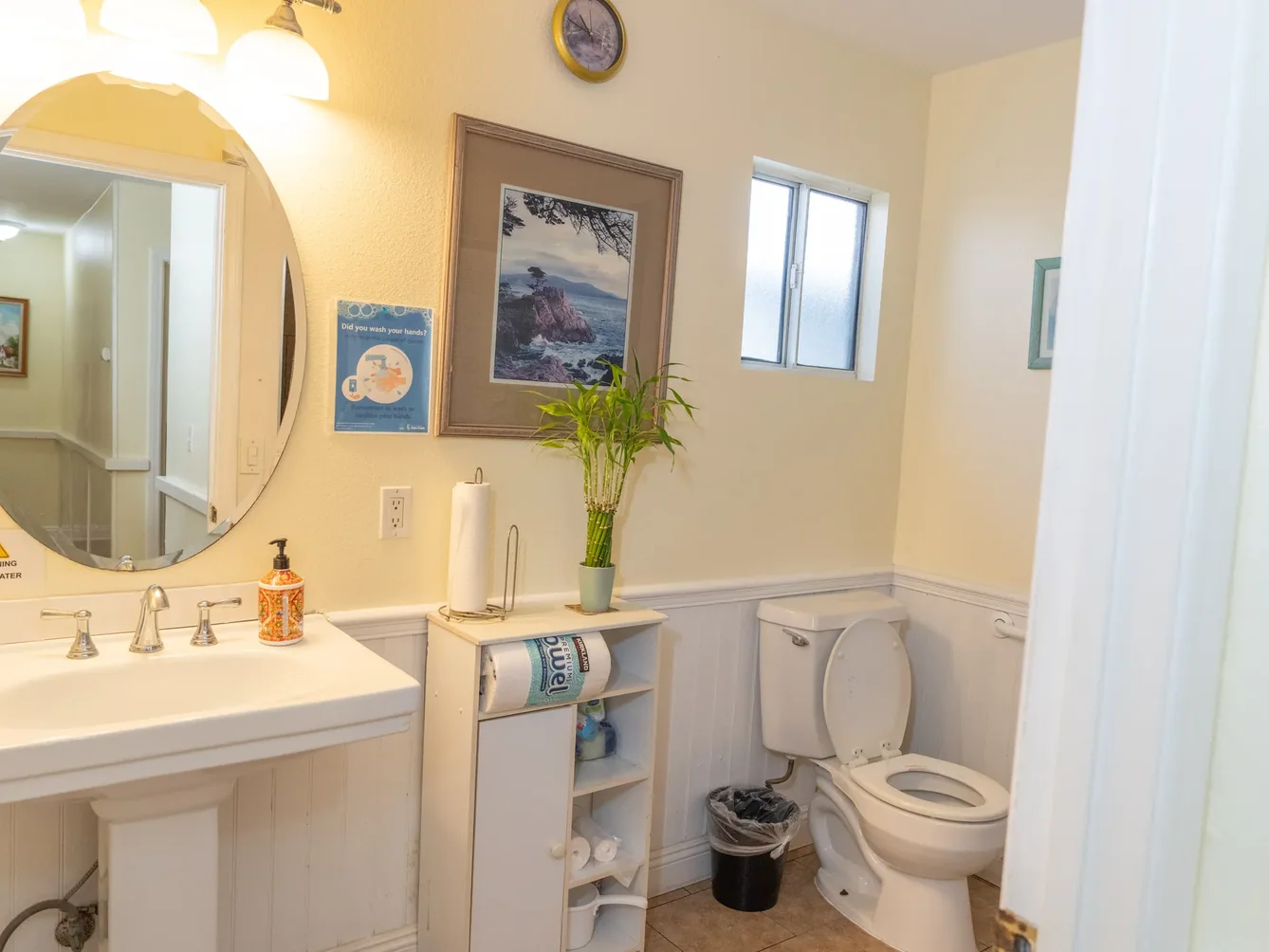 Accessible bathroom with white vanity, toilet, round mirror, and safety features for senior care facility
