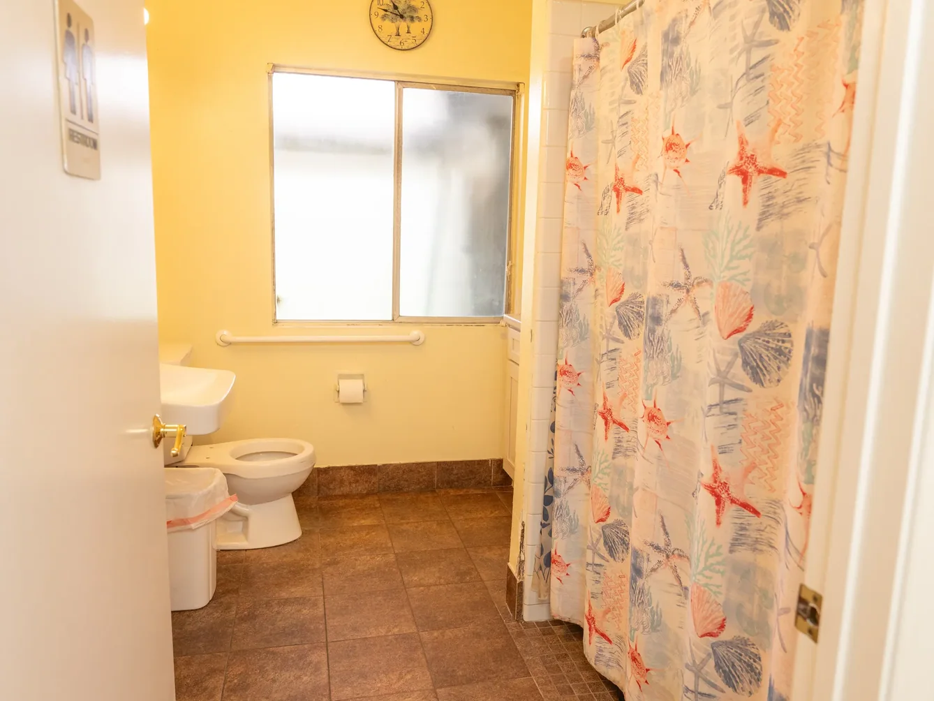 Accessible bathroom with safety grab bar, yellow walls, and ocean-themed shower curtain in residential care facility